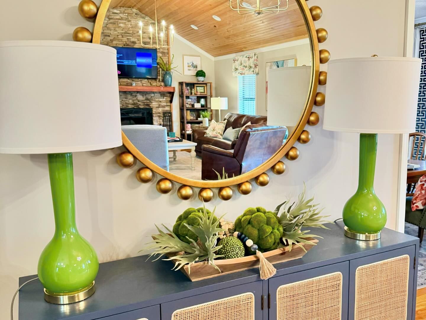 Round Mirror over a blue side table with 2 green accent lamps.